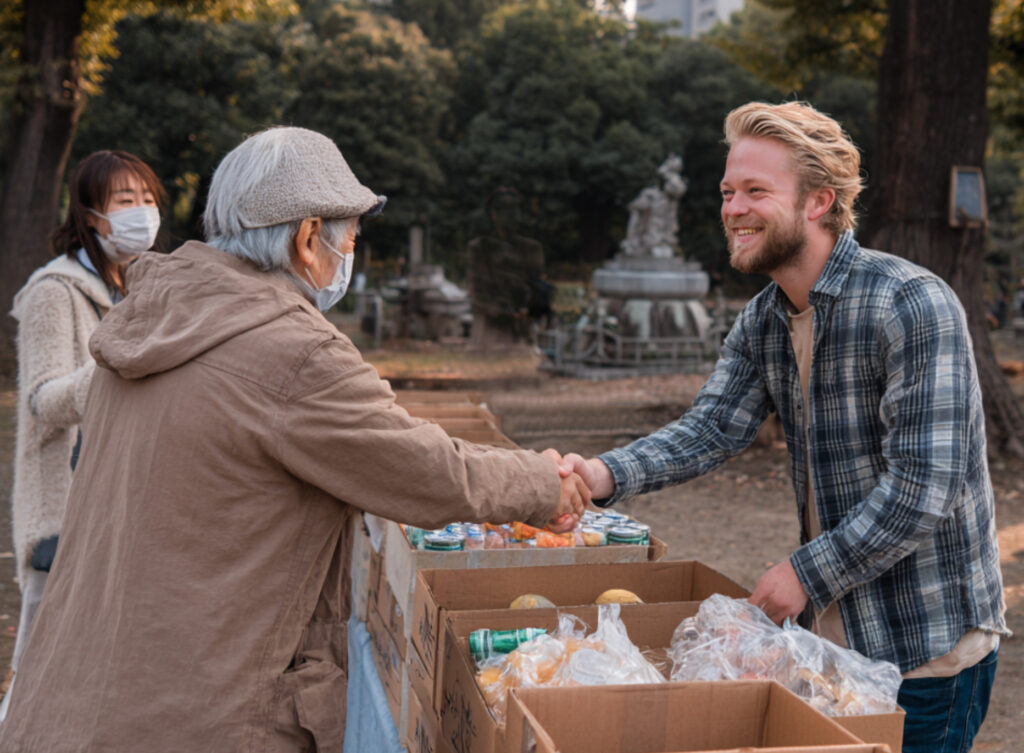 Kozmoz Food Bank volunteer in Osaka park shaking hands with elderly food recipient